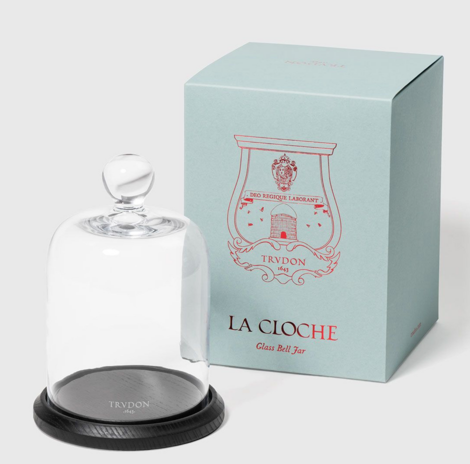 A clear glass cloche with a wooden base, featuring the Trudon brand logo, displayed next to its blue packaging box with the text 'LA CLOCHE' and the brand name.