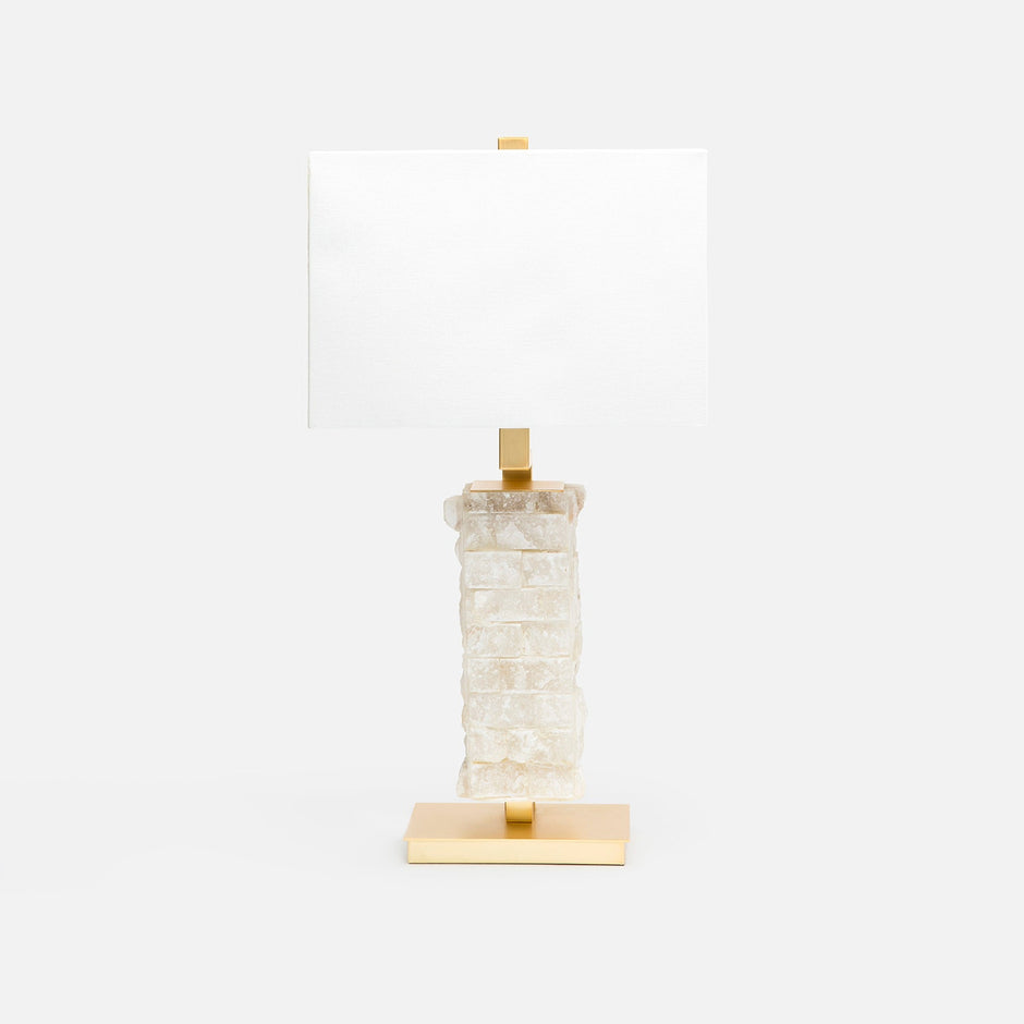 A table lamp with a textured, stacked rough hewn alabaster base in milky white and gold-finished metal accents, including a rectangular gold base and a gold finial, paired with a plain white rectangular shade, set against a solid white background.