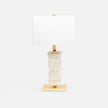 A table lamp with a textured, stacked rough hewn alabaster base in milky white and gold-finished metal accents, including a rectangular gold base and a gold finial, paired with a plain white rectangular shade, set against a solid white background.