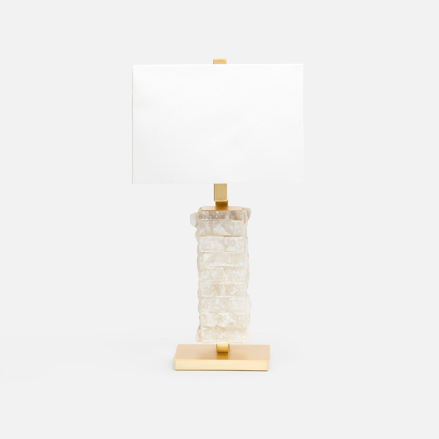 A table lamp with a textured, stacked rough hewn alabaster base in milky white and gold-finished metal accents, including a rectangular gold base and a gold finial, paired with a plain white rectangular shade, set against a solid white background.