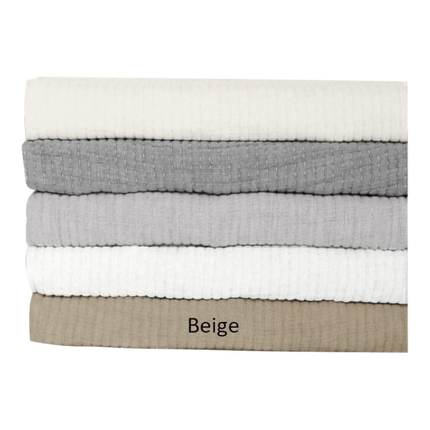 A stack of reversible coverlets in beige, gray, and white, with the label 'Beige' at the bottom.