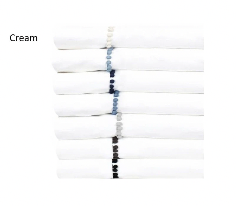 Folded white pillowcases with a decorative border of cream silk pom poms.