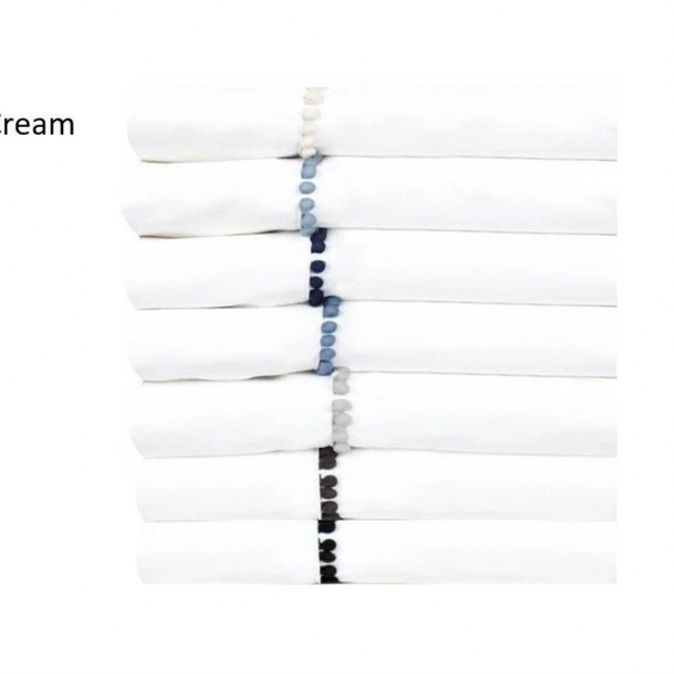 Folded white pillowcases with a decorative border of cream silk pom poms.