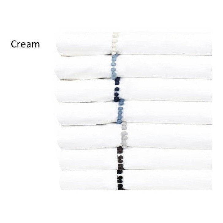 Folded cream-colored sheet set with silk pom poms detail on the edge.