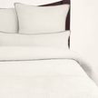 A cream-colored quilt and pillows on a bed, with the brand name 'Avasa' visible on the tag.