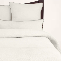 A cream-colored quilt and pillows on a bed, with the brand name 'Avasa' visible on the tag.