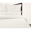A cream-colored, solid patterned quilt displayed on a bed with matching pillows, against a plain background.