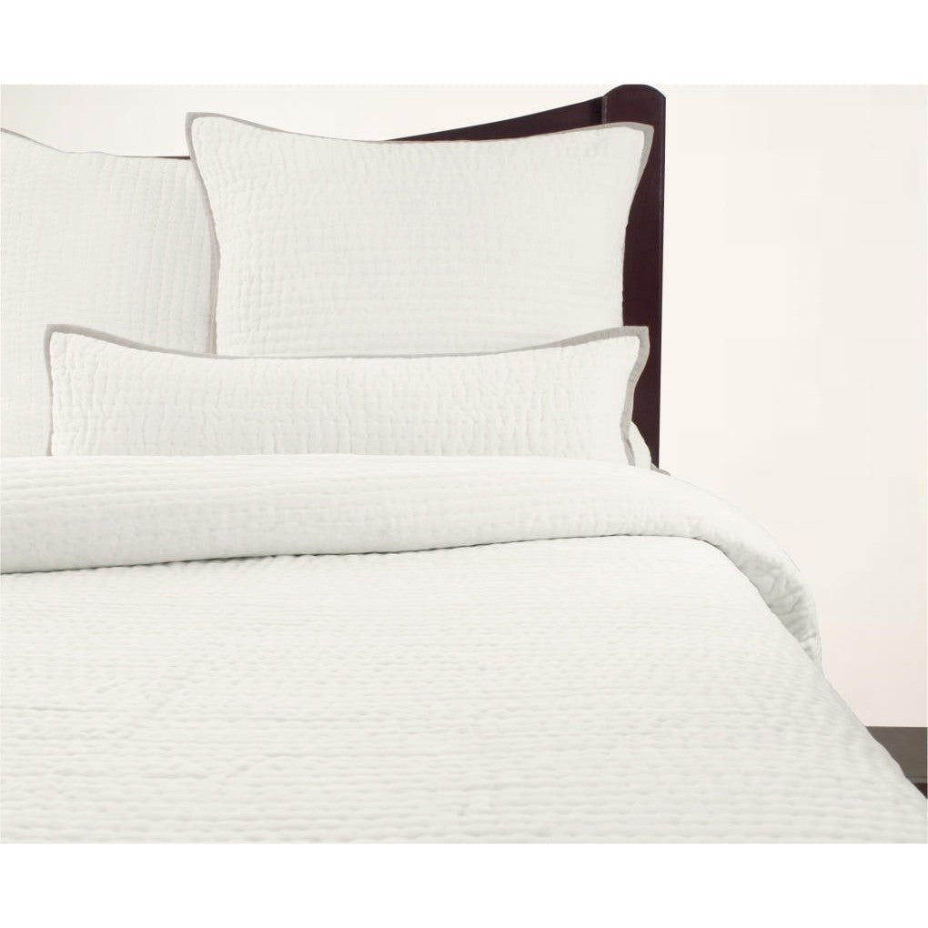 A cream-colored, solid patterned quilt displayed on a bed with matching pillows, against a plain background.