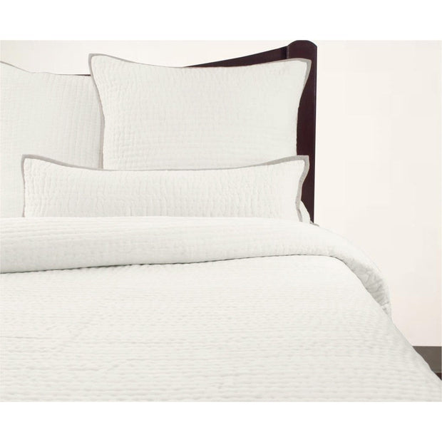 A cream-colored, solid patterned quilt displayed on a bed with matching pillows, against a plain background.
