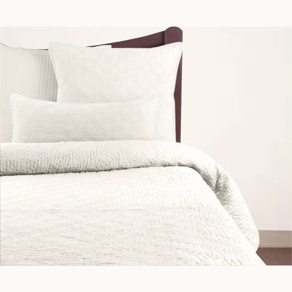 A white quilt with a double diamond pattern on a bed, with coordinating pillowcases.