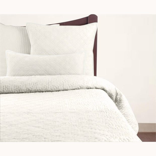 A white quilt with a double diamond pattern on a bed, with coordinating pillowcases.
