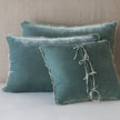 A set of two plush blue pillows with a charmeuse ruffle and ties on a bed.