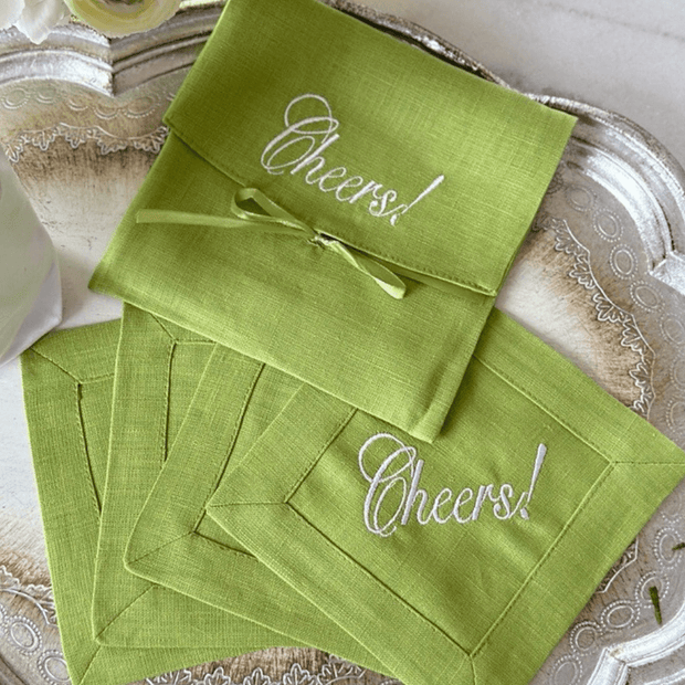 A set of green linen cocktail napkins embroidered with the word 'Cheers' on each