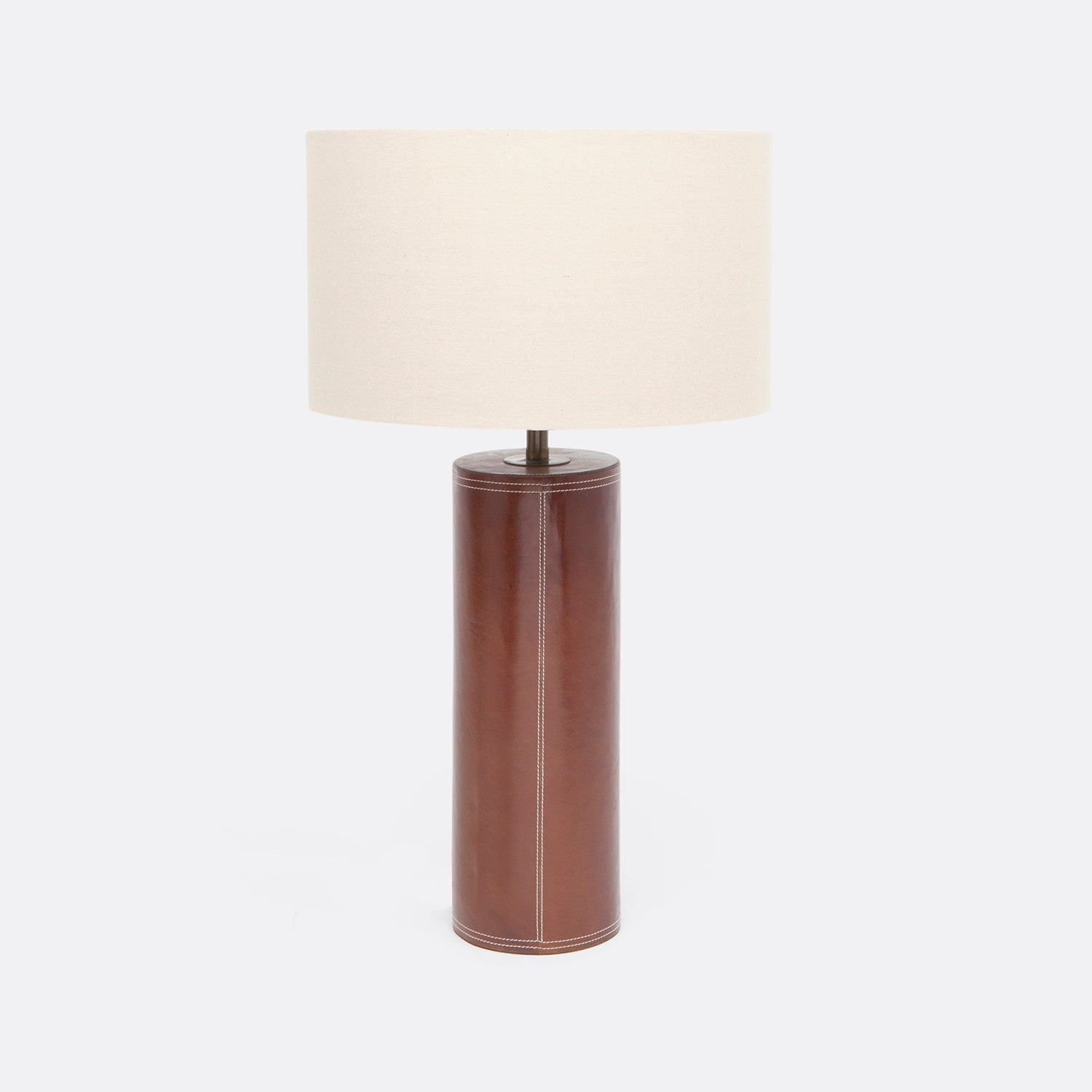 A modern table lamp with a cylindrical leather base and a large, tapered off-white fabric drum shade, shown against a plain light gray background.