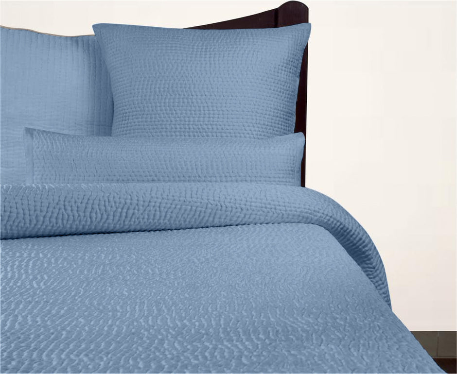 Blue textured bedding set on a bed with pillows and a comforter.