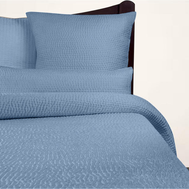 Blue textured bedding set on a bed with pillows and a comforter.
