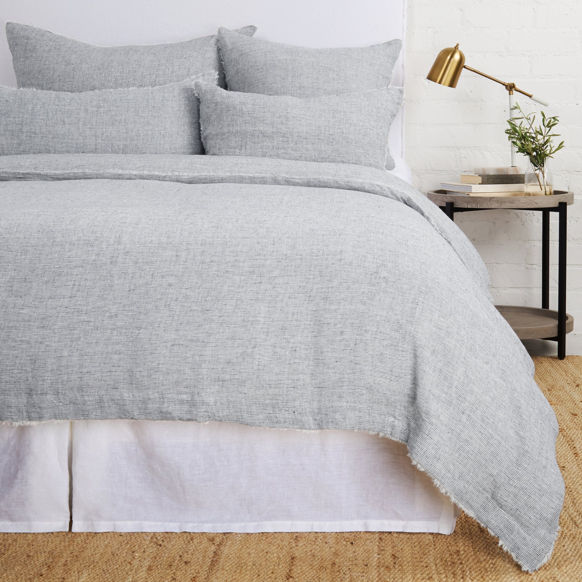 A navy and natural pinstriped linen duvet cover with frayed edges, displayed on a bed with matching pillowcases, in a room setting with bedside table and lamp.