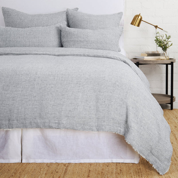 A navy and natural pinstriped linen duvet cover with frayed edges, displayed on a bed with matching pillowcases, in a room setting with bedside table and lamp.