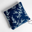 A square-shaped throw pillow with a blue velvet front featuring floral embroidery and a midweight linen back, with a visible drawstring on the side.