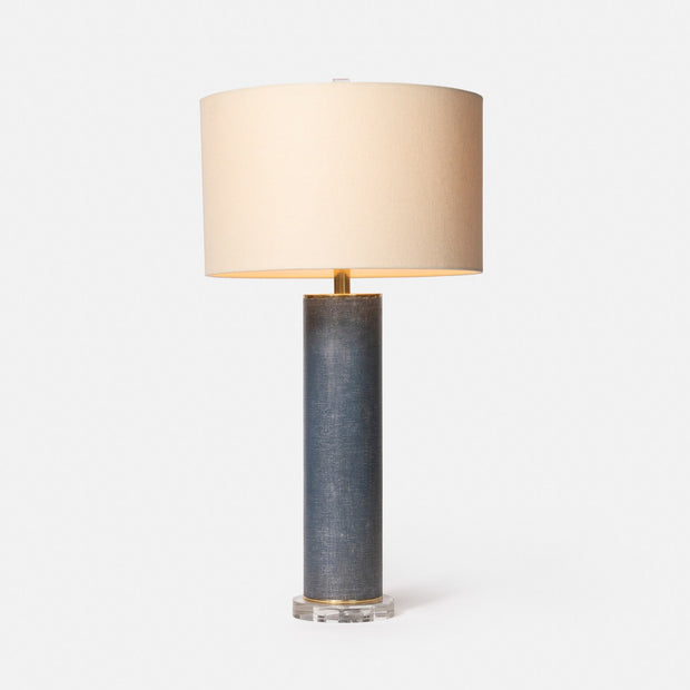 A cylindrical Tavis table lamp with a faux linen covering, brass discs on the top and bottom, and a circular crystal base, accompanied by a beige lampshade.
