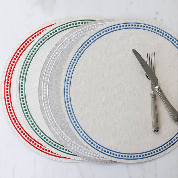 A set of round placemats with dotted patterns around the edges, displayed in red, white, and blue colors, with a fork and knife placed on top of the white one.