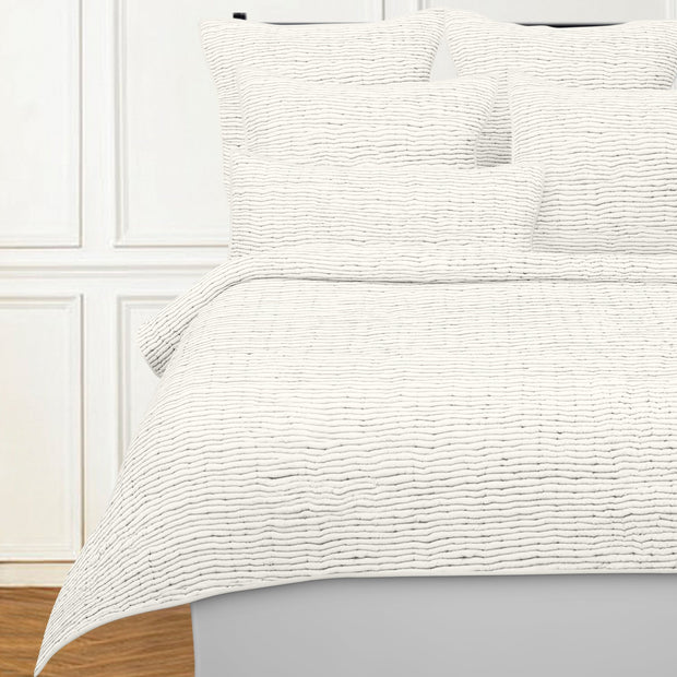 Textured white bedding set on a bed with a wooden floor and white wall background