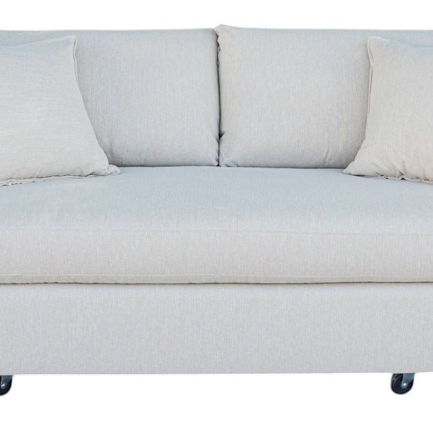 A 'Verellen Thibaut Sofa Amelia Bisque' with beige upholstery, featuring slightly tapered arms, low tight seat, and plush back cushions, on caster wheels.