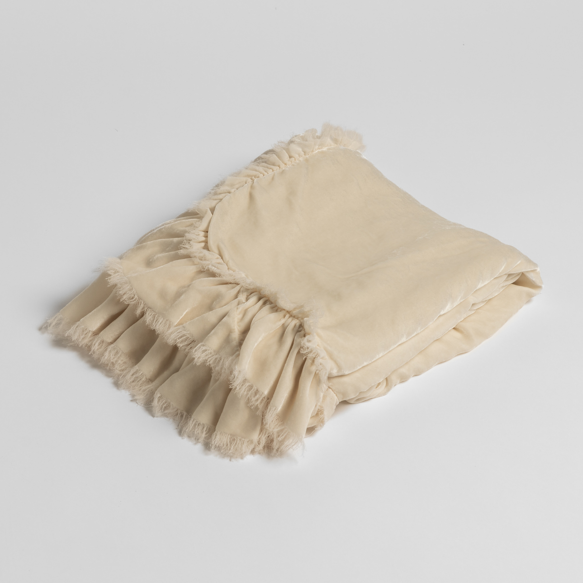 Cream-colored Bella Notte Loulah throw blanket displayed casually on a cozy sofa with soft, luxurious fabric visible.