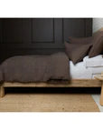 Wooden bed frame with a dark brown blanket and white pillows against a dark wall.