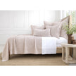 Neatly made bed with beige quilt and pillows in a bright bedroom.