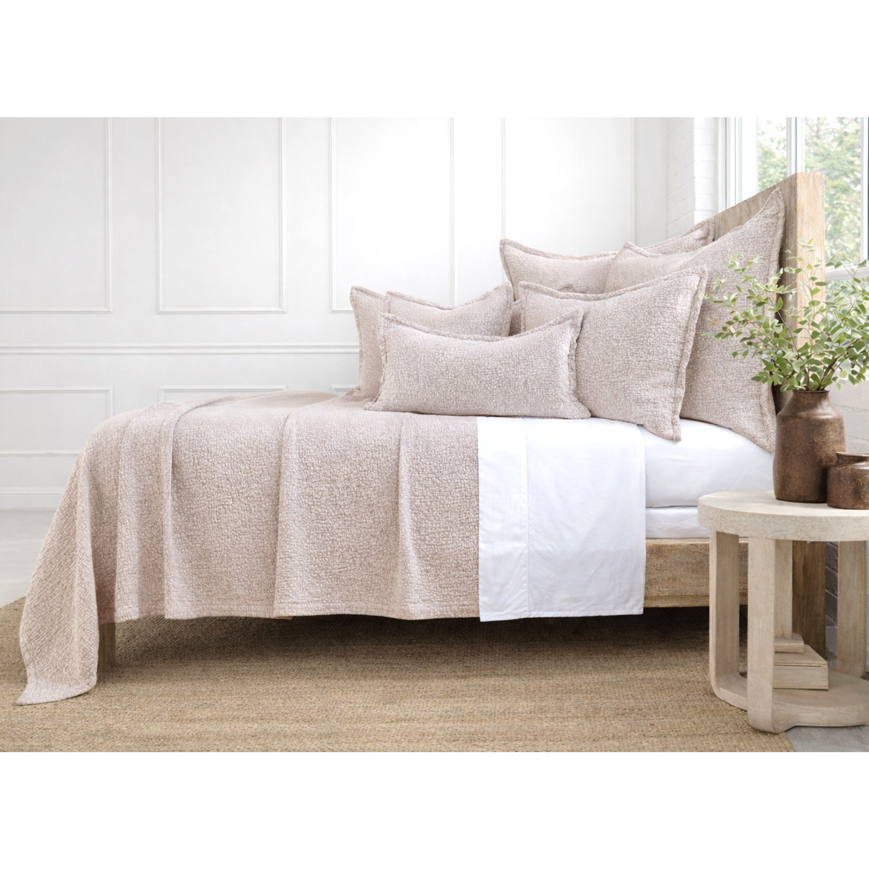 Neatly made bed with beige quilt and pillows in a bright bedroom.