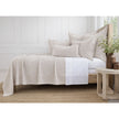 Neatly made bed with beige and white bedding in a bright bedroom.