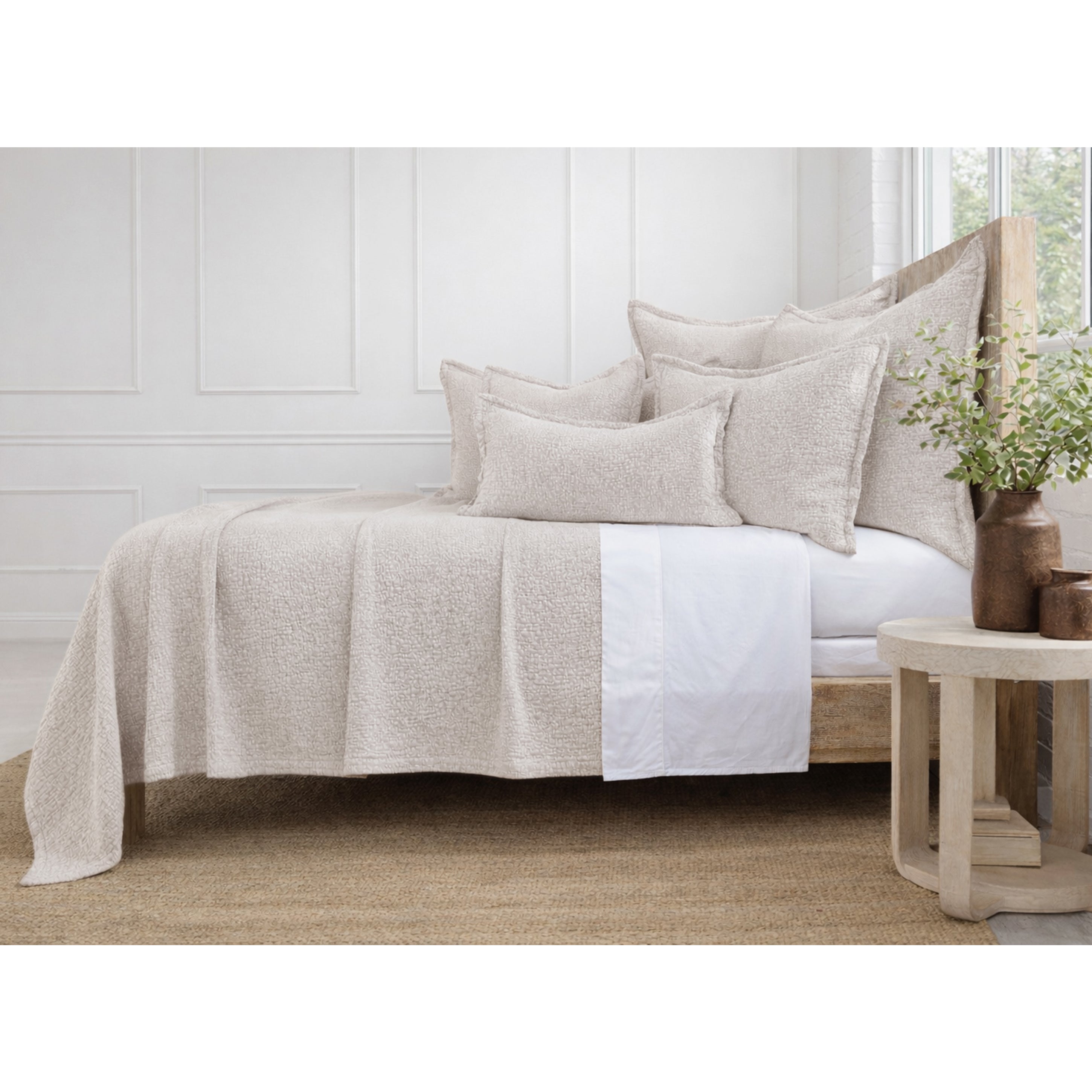 Neatly made bed with beige and white bedding in a bright bedroom.