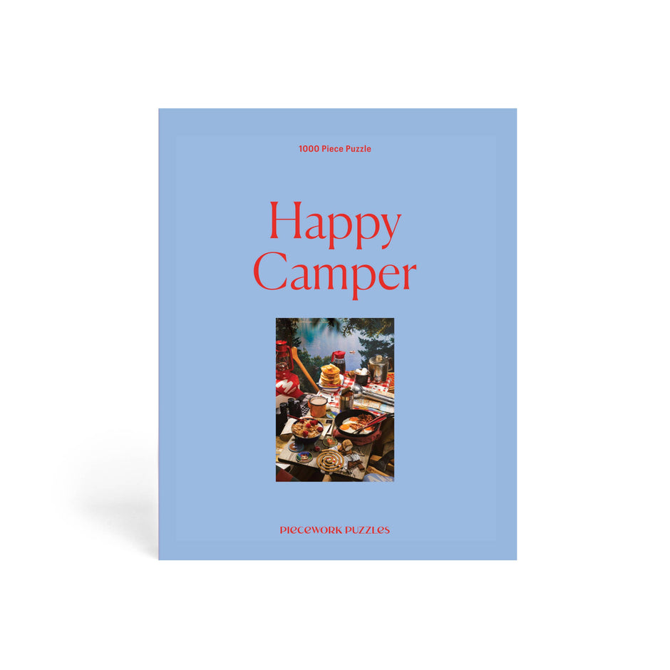 1000-piece Happy Camper puzzle by Piecework featuring a colorful camping scene with tents, trees, and a cheerful outdoor setting.
