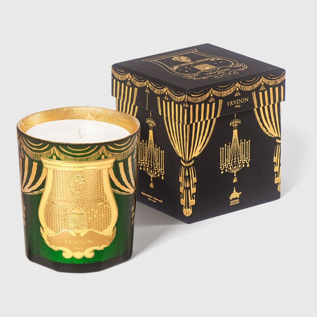 A Trudon holiday candle with a green and gold design, accompanied by its black and gold packaging box with similar designs.