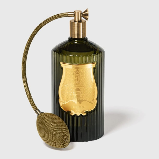 A green glass room spray bottle with a gold-colored lid and a gold pump, hand made in France.